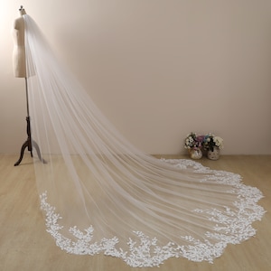 Peut inclure: Un long voile de mari&eacute;e en tulle blanc avec une d&eacute;licate bordure en dentelle florale. Le voile est drap&eacute; sur un mannequin et coule sur le sol.