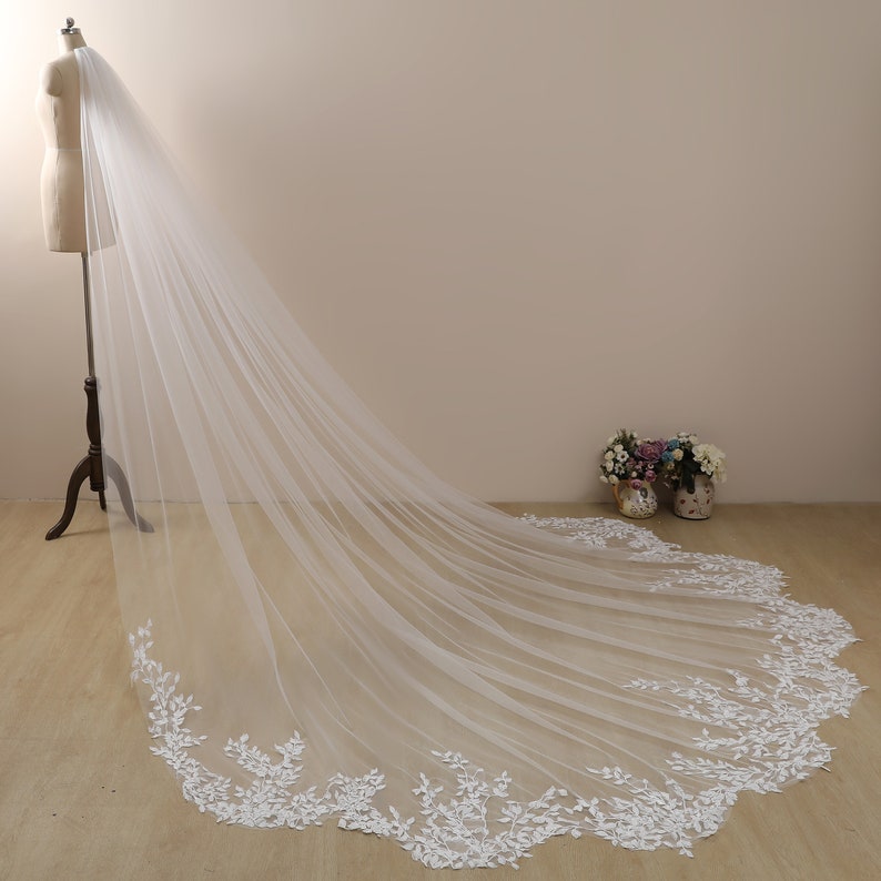 Peut inclure: Un long voile de mari&eacute;e en tulle blanc avec une d&eacute;licate bordure en dentelle florale. Le voile est drap&eacute; sur un mannequin et coule sur le sol.