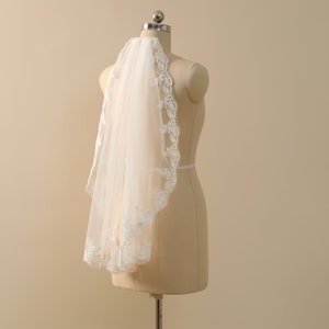 May include: A white bridal veil with a delicate lace trim. The veil is displayed on a mannequin.
