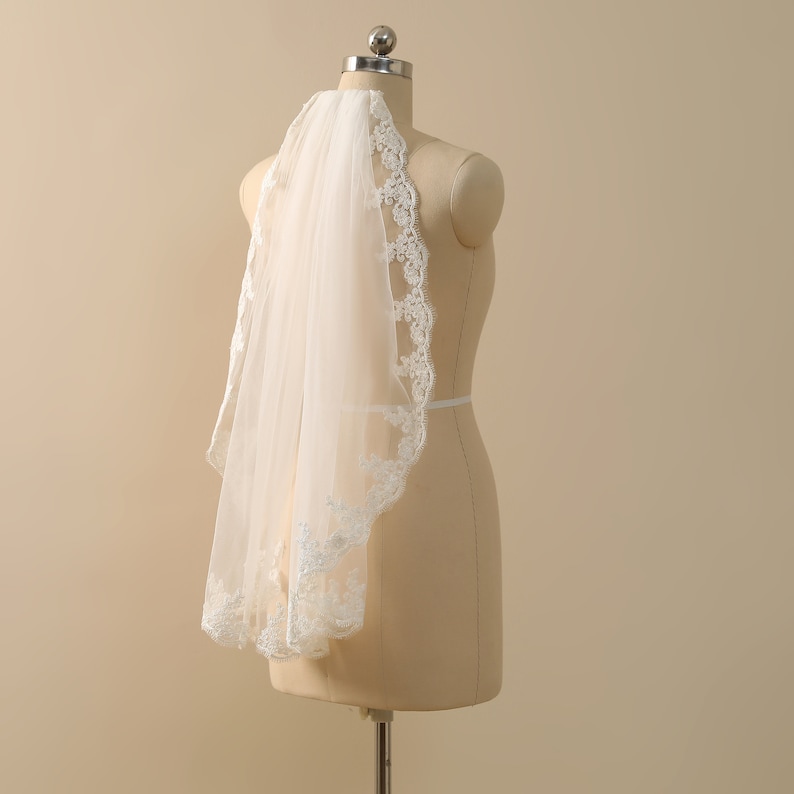 May include: A white bridal veil with a delicate lace trim. The veil is displayed on a mannequin.