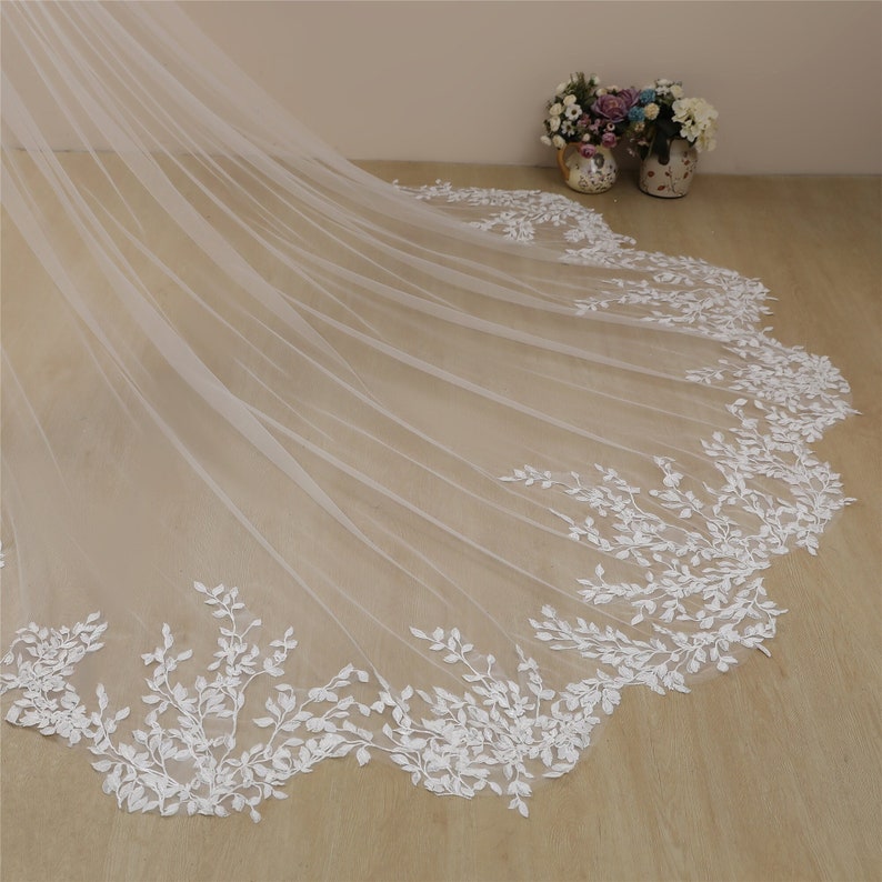 Peut inclure: Un voile de mari&eacute;e en tulle blanc avec une bordure en dentelle florale d&eacute;licate. La dentelle pr&eacute;sente un motif de petites feuilles et branches blanches.