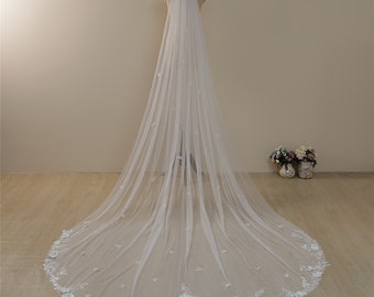 May include: A long white bridal veil with delicate floral embroidery. The veil is made of soft tulle and has a scalloped edge.