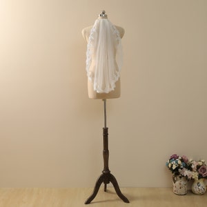 May include: A white bridal veil with a delicate lace trim. The veil is displayed on a mannequin and is made of soft tulle.