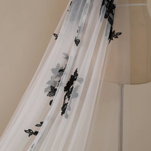 May include: White tulle fabric with black floral embroidery. The fabric is draped over a dress form.