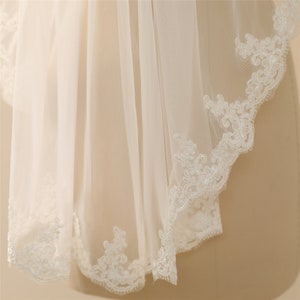 May include: A white bridal veil with a delicate lace trim. The lace is a floral pattern with a scalloped edge.