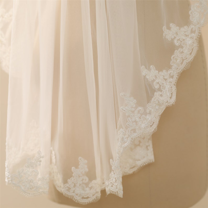 May include: A white bridal veil with a delicate lace trim. The lace is a floral pattern with a scalloped edge.