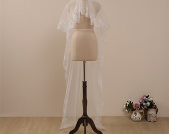 May include: A white bridal veil with a delicate lace trim. The veil is displayed on a wooden stand.