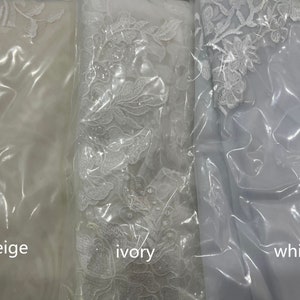 May include: Three swatches of fabric in beige, ivory, and white. Each swatch has a floral lace pattern.