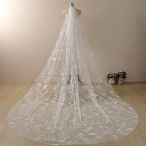 May include: A white bridal veil featuring delicate floral lace embroidery. The veil is long and flowing, with a soft, sheer texture.
