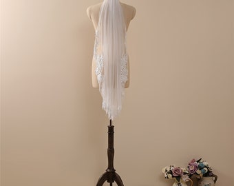 May include: A white bridal veil with a delicate lace trim. The veil is displayed on a mannequin and is made of soft tulle.