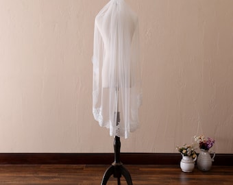 May include: A white bridal veil with a lace trim. The veil is displayed on a mannequin.