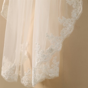 May include: White bridal veil with a delicate lace trim. The lace features a floral pattern.