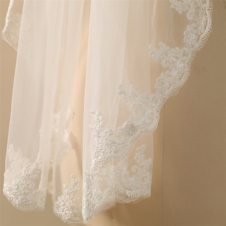 May include: White bridal veil with a delicate lace trim. The lace features a floral pattern.