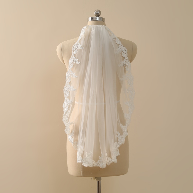 May include: A white bridal veil with a delicate lace trim. The veil is made of soft tulle and is designed to be worn over the head.