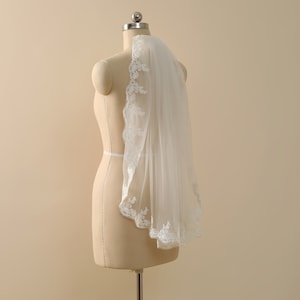 May include: A white bridal veil with a delicate lace trim. The veil is draped over a dress form.