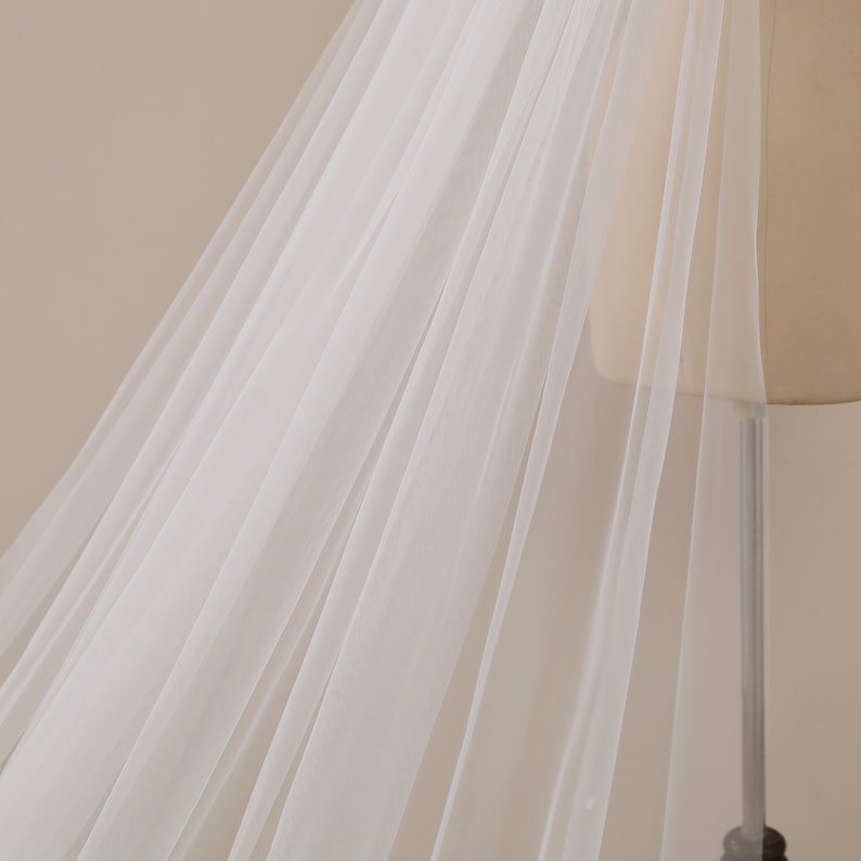 Peut inclure: Un voile de mari&eacute;e en tulle blanc avec un design long et fluide. Le voile est drap&eacute; sur un mannequin et a une texture douce et d&eacute;licate.