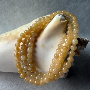 May include: A multi-strand necklace composed of smooth, round, translucent golden-yellow beads. The beads exhibit a polished finish with subtle variations in color and internal texture, strung together to form a continuous circular loop.