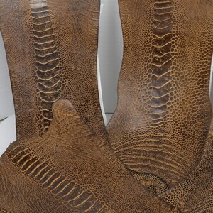 May include: Two pieces of brown ostrich leather with a textured pattern. The leather is soft and supple, and it has a natural, rustic look.