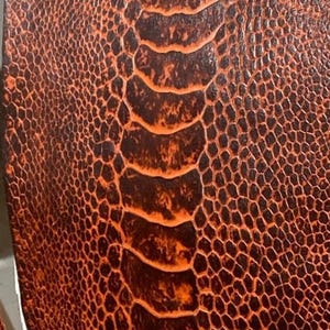 Pode incluir: Close-up de um couro laranja texturizado com um padrão marrom escuro. O couro tem uma aparência escamosa, reptiliana.