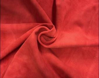 May include: Close-up of a vibrant red fabric with a soft, suede-like texture. The material is artfully draped, creating folds and shadows that highlight its rich color and tactile quality. The fabric's surface appears smooth and inviting.