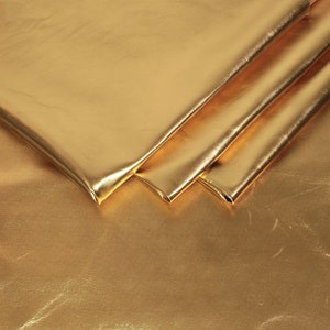 May include: Close-up of a folded piece of gold metallic fabric. The fabric has a smooth, shiny surface.