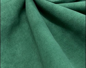 May include: Close-up of a folded piece of emerald green fabric. The material has a soft, suede-like texture with subtle variations in tone, creating depth. The folds and curves of the fabric are visible, highlighting its drape.