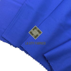 Puede incluir: Primer plano de una tela azul vibrante con textura y pliegues visibles. La tela es de color liso, con el texto "LA CITY FABRICS" y un logotipo en el centro. La tela parece ser un material textil.