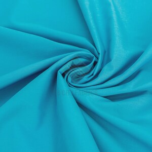 Puede incluir: Una tela de color turquesa vibrante con una textura suave y mate, con pliegues profundos y fluidos que crean un patrón dinámico y arremolinado. El material está drapeado en una espiral central, mostrando el color sólido y la superficie flexible.