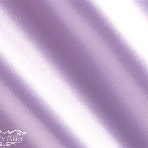 May include: A close-up of a smooth, silky fabric in a light lavender colour. The fabric is draped and folded, creating soft, flowing lines.