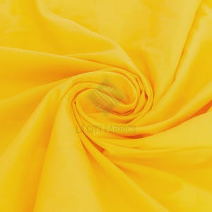 Puede incluir: Una tela de color amarillo vibrante con una superficie lisa y de color sólido, con pliegues suaves y fluidos que crean un patrón circular en espiral. El texto LA CITY FABRICS es visible como una marca de agua semitransparente en el centro.