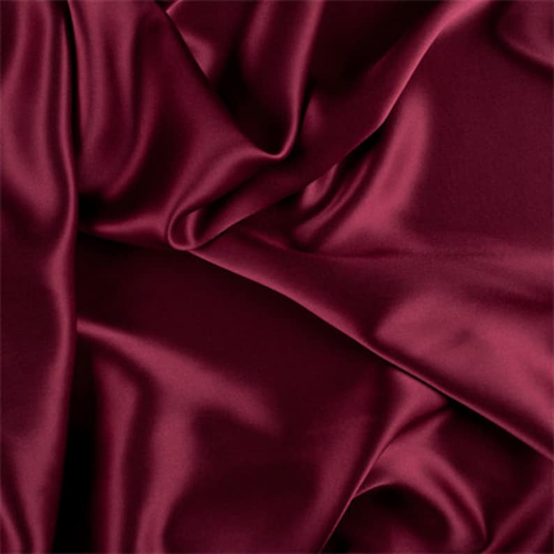 May include: Close-up of a deep red satin fabric with soft, flowing folds. The fabric has a smooth, luxurious texture.