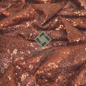 May include: Close-up of a copper-colored fabric with sequins. The fabric is textured and has a shimmery finish.