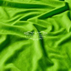 May include: A close-up of a bright green fabric with a soft, smooth texture. The fabric is draped and folded, creating a sense of movement and flow. The fabric is perfect for sewing projects, crafts, and home decor.