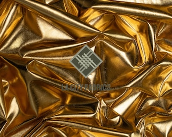 May include: Close-up of a shiny, golden fabric with a metallic sheen. The fabric is heavily draped, creating folds and shadows that reflect light. The LA City Fabrics logo is visible in the centre.
