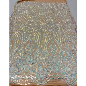 Op de afbeelding: Iridescent witte en blauwe pailletten op een transparante stof met een bloemenpatroon. De stof is perfect voor het maken van jurken, rokken en andere kleding.