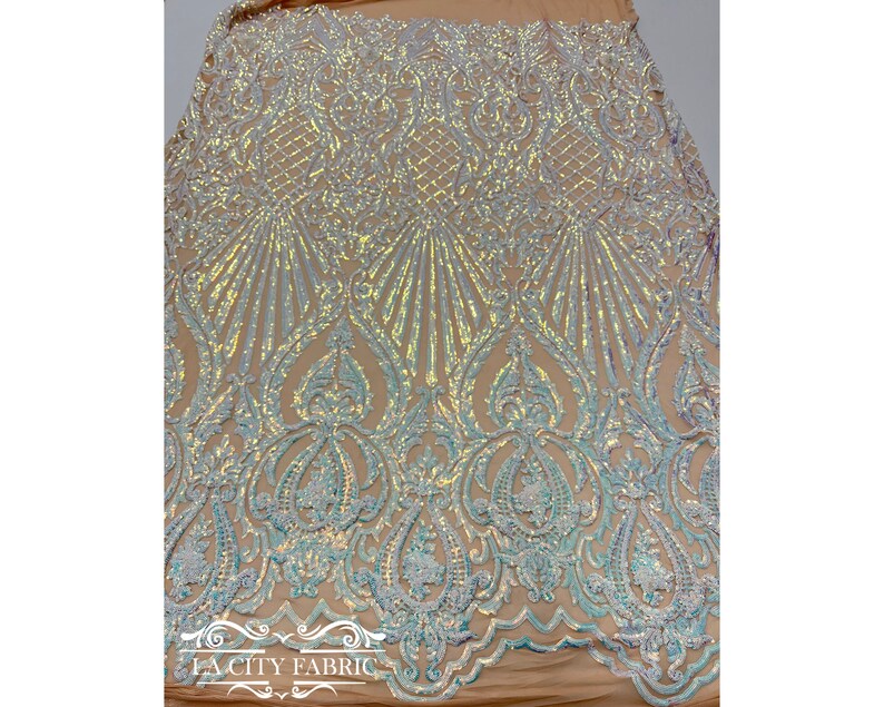 Op de afbeelding: Iridescent witte en blauwe pailletten op een transparante stof met een bloemenpatroon. De stof is perfect voor het maken van jurken, rokken en andere kleding.