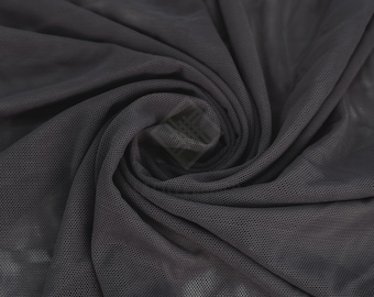 May include: A dark charcoal gray mesh fabric featuring a fine, semi-sheer hexagonal grid pattern. The material is gathered into a central spiral, creating deep, flowing folds and shadows that highlight the texture and transparency of the textile.