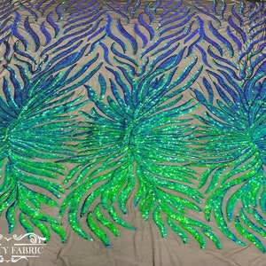 Op de afbeelding: Groene en blauwe, iriserende pailletten op een zwarte mesh-stof. De pailletten zijn gerangschikt in een draaiende vorm, wat een dynamisch en opvallend ontwerp creëert.
