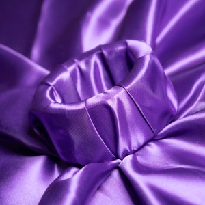 Pode incluir: Um close-up de um tecido de cetim roxo enrugado para formar um círculo. O tecido é liso e brilhante, com um toque suave e luxuoso.