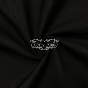 Pode incluir: Tecido preto com textura lisa. O tecido está dobrado e drapeado, mostrando sua natureza suave e fluida. O texto "LA CITY FABRIC" está impresso em branco no tecido.