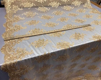 May include: Gold floral lace fabric with a delicate pattern on a sheer mesh background. The fabric is shown with a ruler for scale.