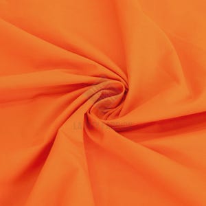 Puede incluir: Una tela de color naranja vibrante y sólido con una textura suave y mate. El material está recogido en el centro, creando pliegues suaves y fluidos con sombras profundas que resaltan el color naranja brillante y uniforme en la superficie.