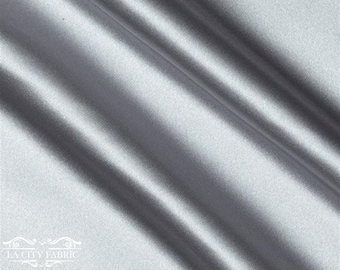 May include: A smooth, silver satin fabric with a subtle sheen. The fabric is folded in a diagonal pattern, showcasing its drape and texture.