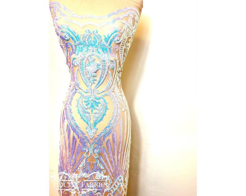 Op de afbeelding: Iridescent blauwe en paarse pailletten op een transparante mesh stof. De pailletten zijn gerangschikt in een bloemenpatroon. De stof is perfect voor het maken van een jurk of ander kledingstuk.