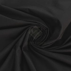 May include: A solid black fabric with a smooth, matte texture, arranged in a central spiral swirl pattern that creates deep, soft folds and shadows across the surface. A faint, semi-transparent logo reading LA CITY FABRICS is visible.