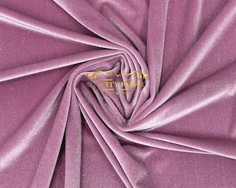 Puede incluir: Primer plano de una tela de terciopelo suave de color rosa con un brillo sutil. La tela está doblada y drapeada, mostrando su textura y caída.
