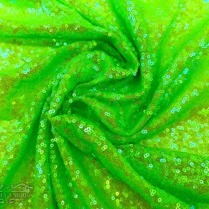 Puede incluir: Primer plano de una tela verde brillante con lentejuelas iridiscentes. La tela está recogida y doblada, mostrando la textura y el brillo de las lentejuelas.