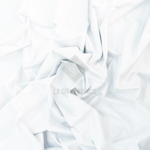 May include: A solid white fabric with a smooth, matte texture, featuring deep folds and creases that create a dynamic play of light and shadow across the surface. A semi-transparent watermark with the text LA CITY FABRICS is centered.