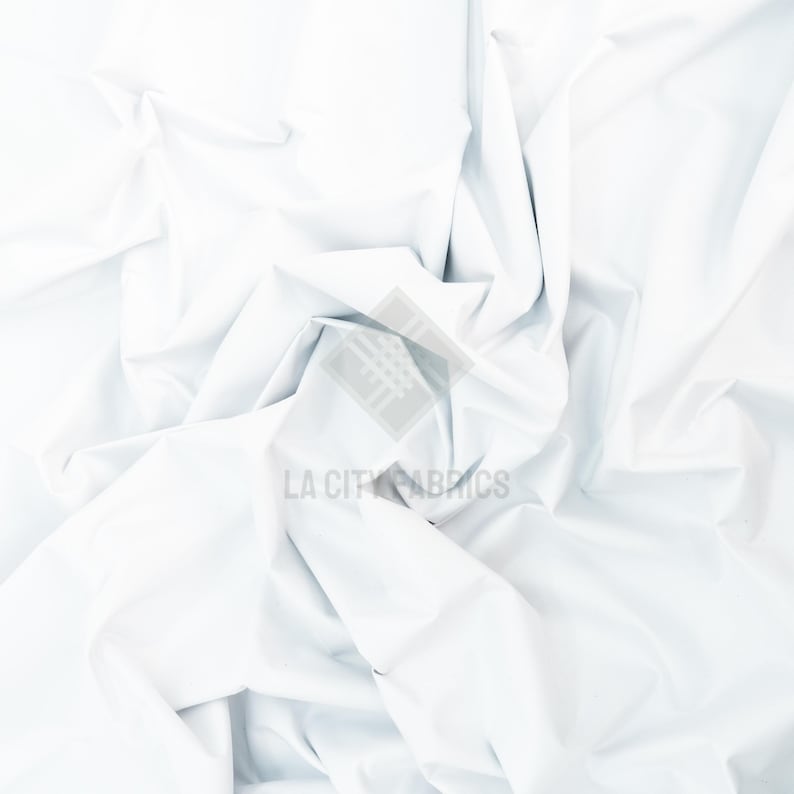 May include: A solid white fabric with a smooth, matte texture, featuring deep folds and creases that create a dynamic play of light and shadow across the surface. A semi-transparent watermark with the text LA CITY FABRICS is centered.