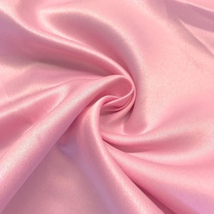 May include: Close-up of a soft, pink satin fabric with a smooth, silky texture. The fabric is draped and folded, creating a luxurious and elegant look.
